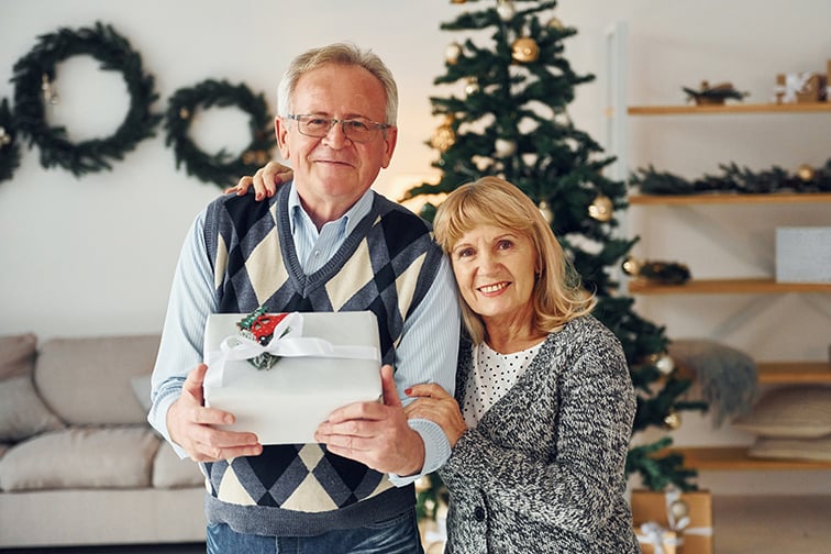 A senior man and a woman standing in front of the Christmas tree.